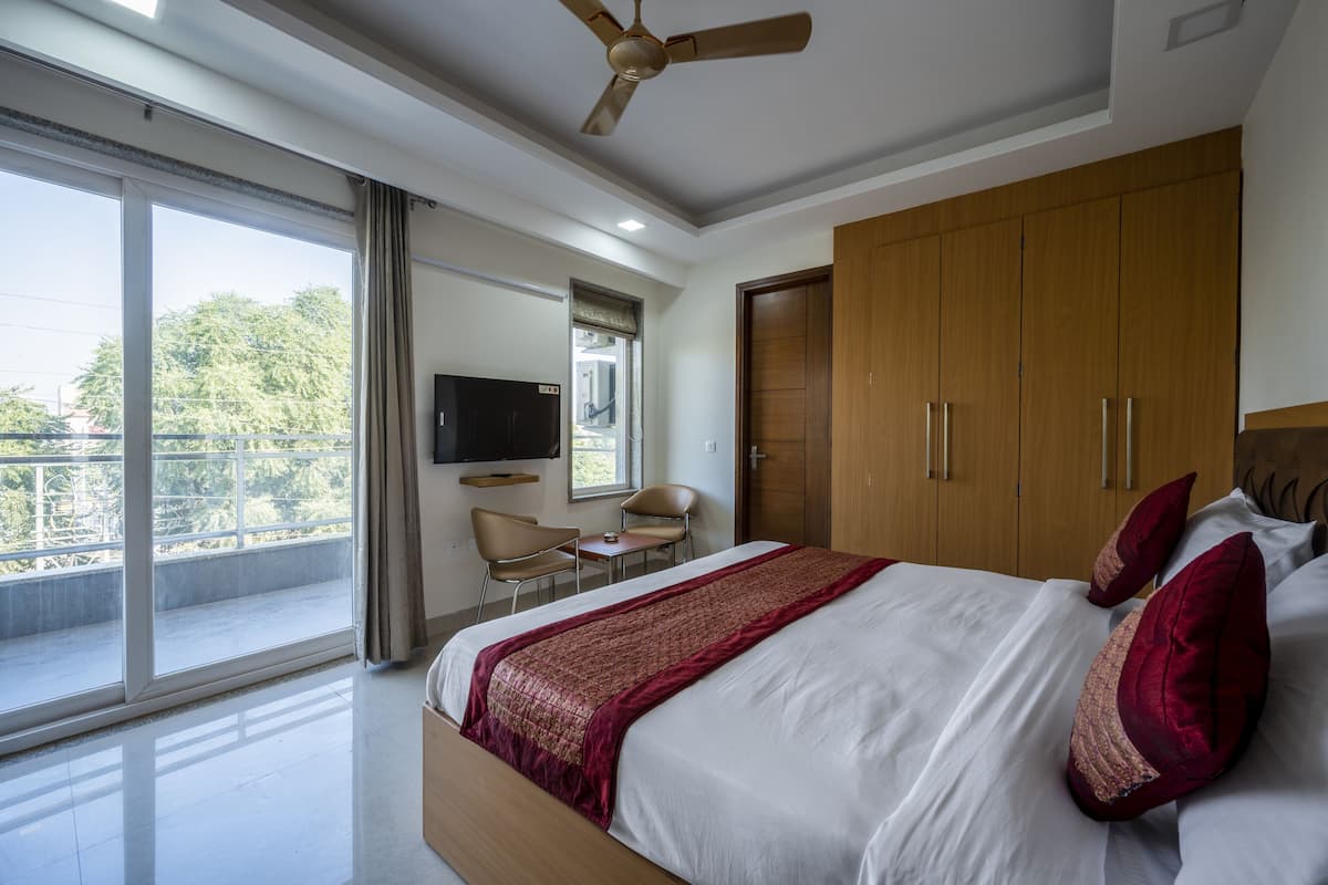 Un dormitorio con una cama grande, un armario de madera, un ventilador de techo, un televisor montado en la pared y un balcón con vistas a árboles.