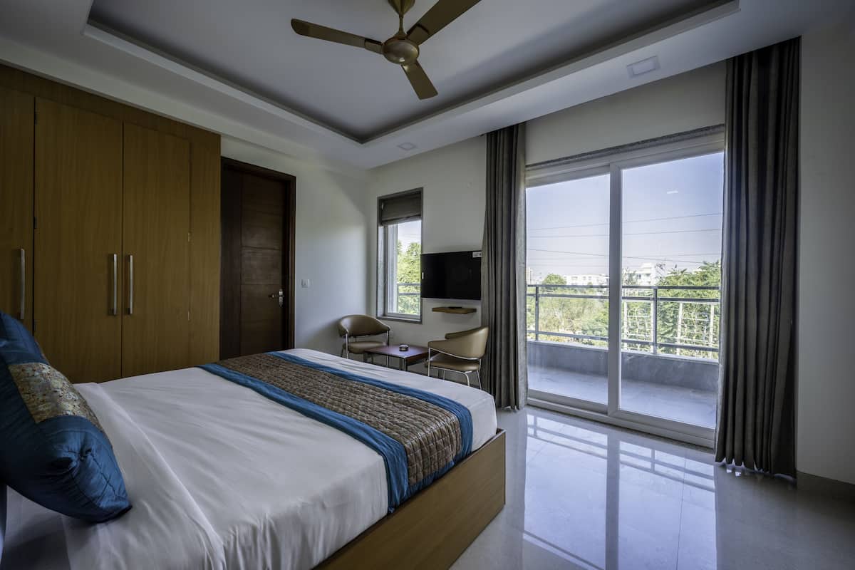 Habitación de hotel moderna con una cama grande, ventilador de techo, televisión y balcón con vistas a la ciudad.