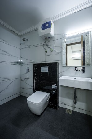 Ein Badezimmer mit einer weißen Toilette, einer schwarzen Duschkabine aus Marmor, einem weißen Waschbecken und einem Spiegel darüber.