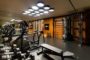 Un gimnasio con varias máquinas de ejercicio, una banca y un espejo grande.