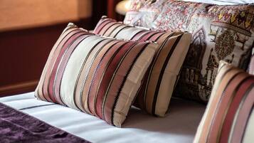 Una cama con almohadillas a rayas y una colcha estampada, una lámpara con pantalla color beige y una pared decorada con un diseño.