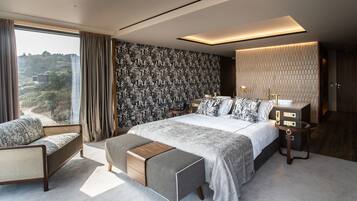 A modern bedroom with a large bed, a sofa, a bedside table, and a view of a mountainous landscape.