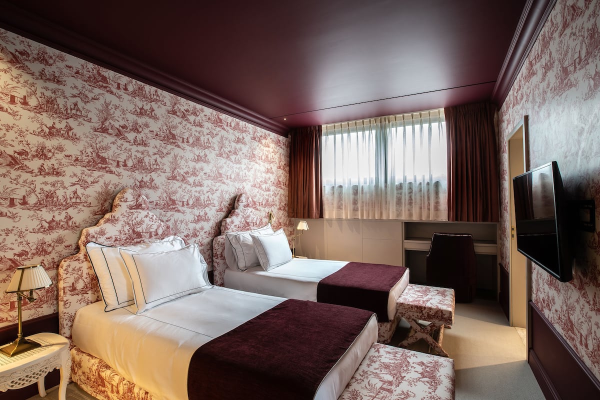 Une chambre d’hôtel avec deux lits, une télévision, un bureau et une fenêtre avec des rideaux.