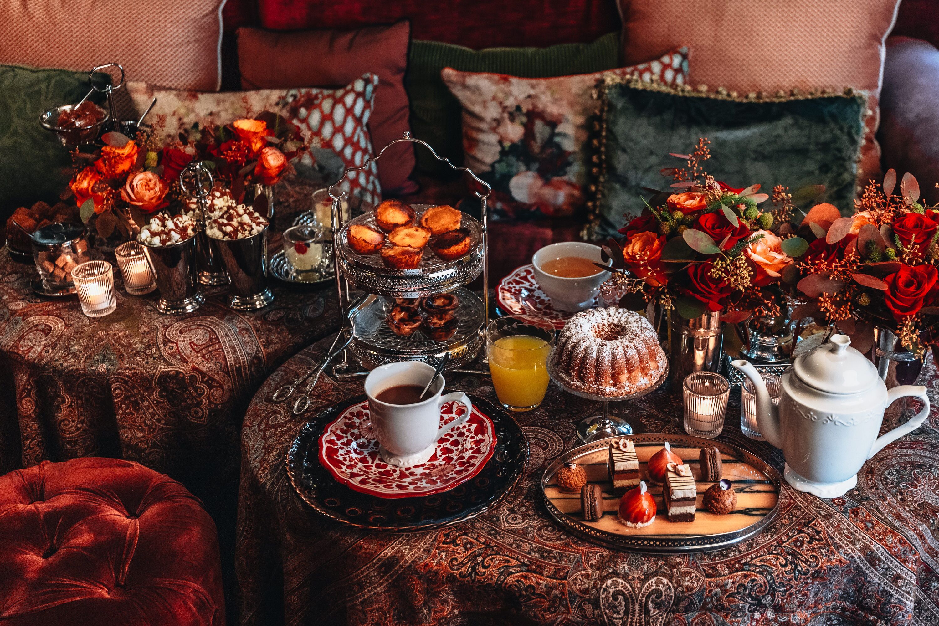 Uma mesa posta com doces, chá e um arranjo floral.