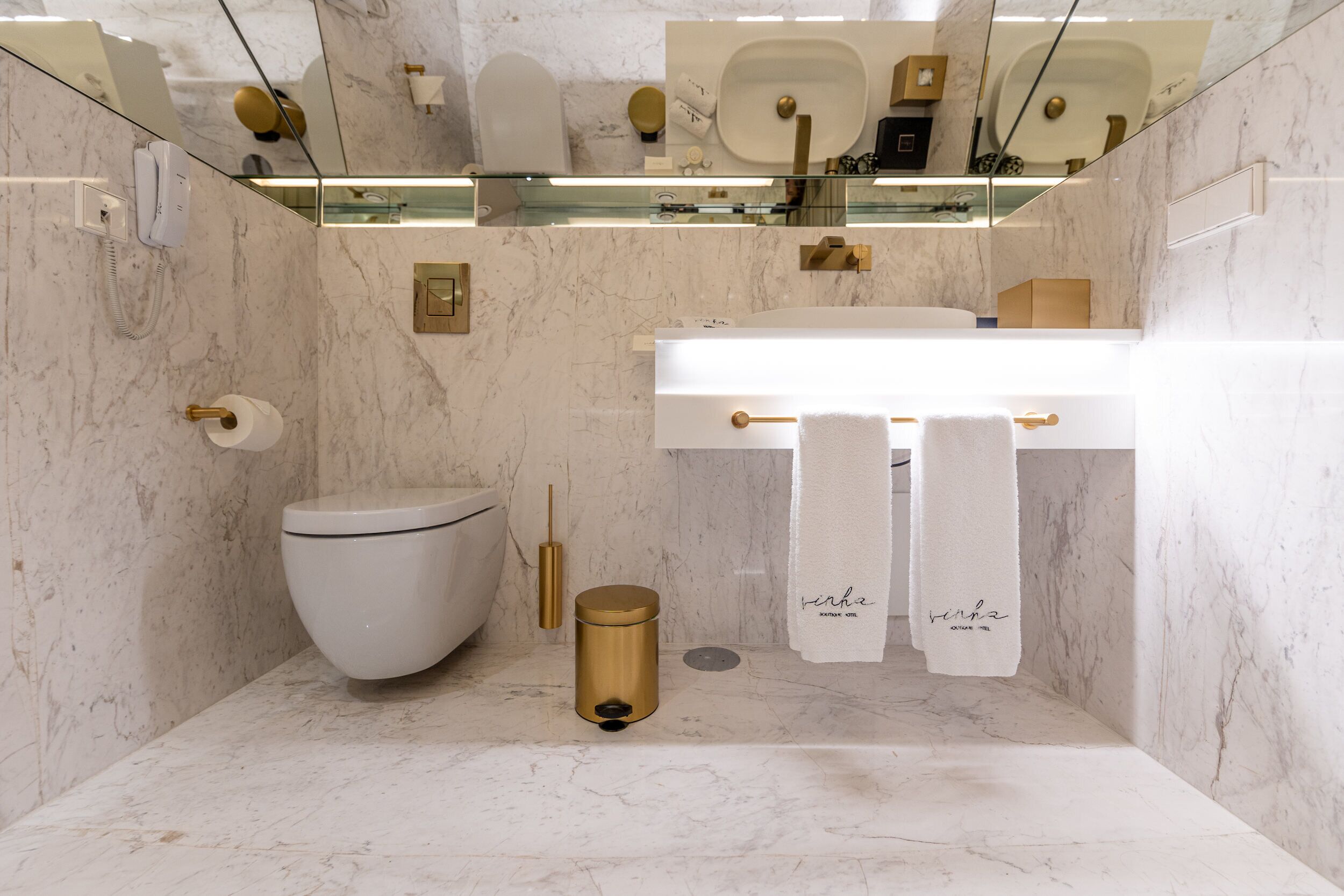A modern bathroom with a marble floor, a white toilet, a gold bidet, and a white sink with a towel rack.