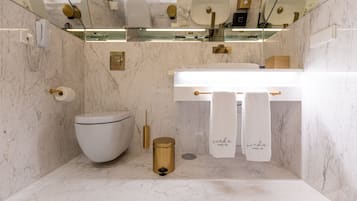 A modern bathroom with a marble floor, a white toilet, a gold bidet, and a white sink with a towel rack.
