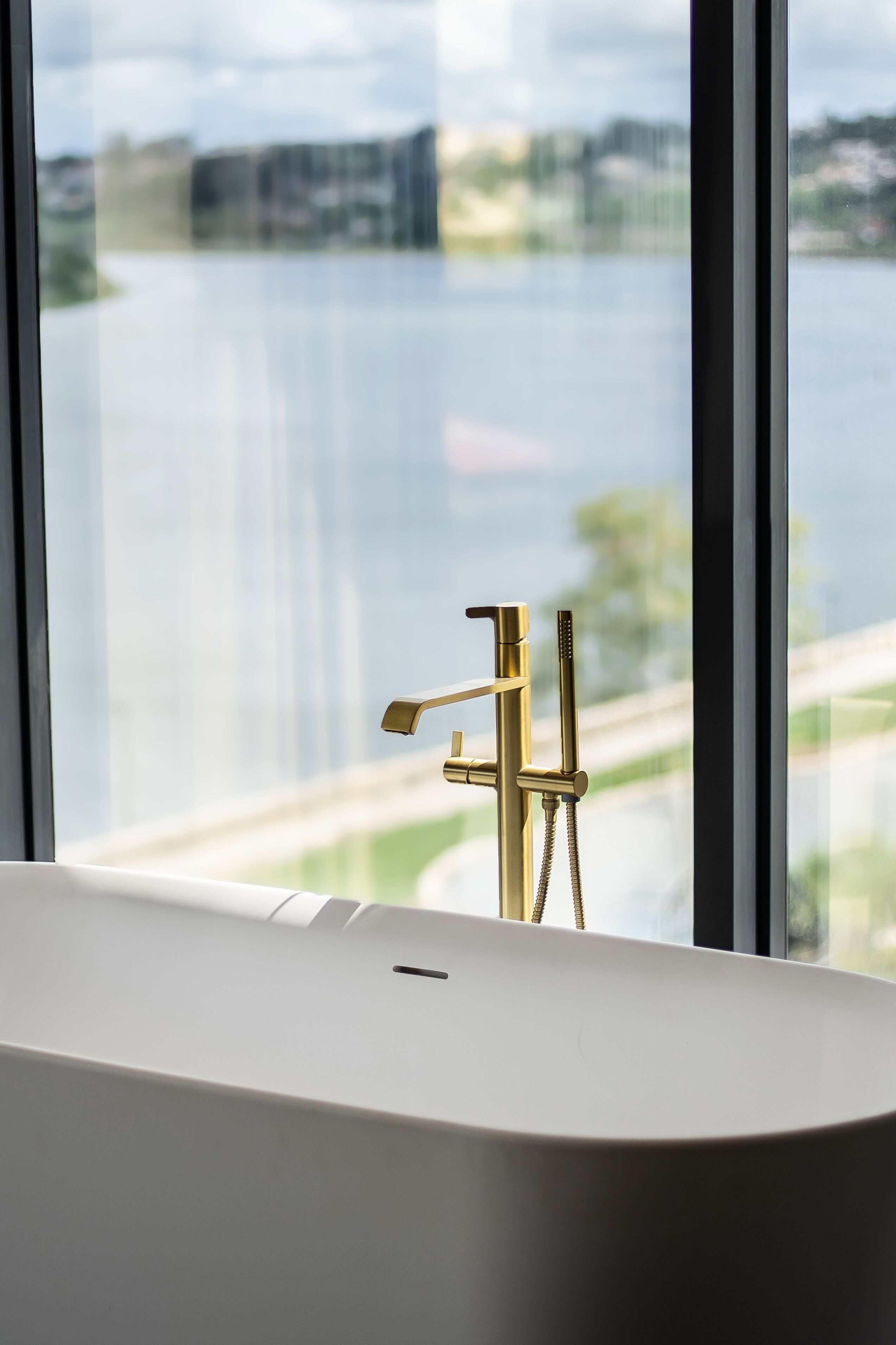 A bathroom with a bathtub, a gold faucet, and a view of a body of water through a window.