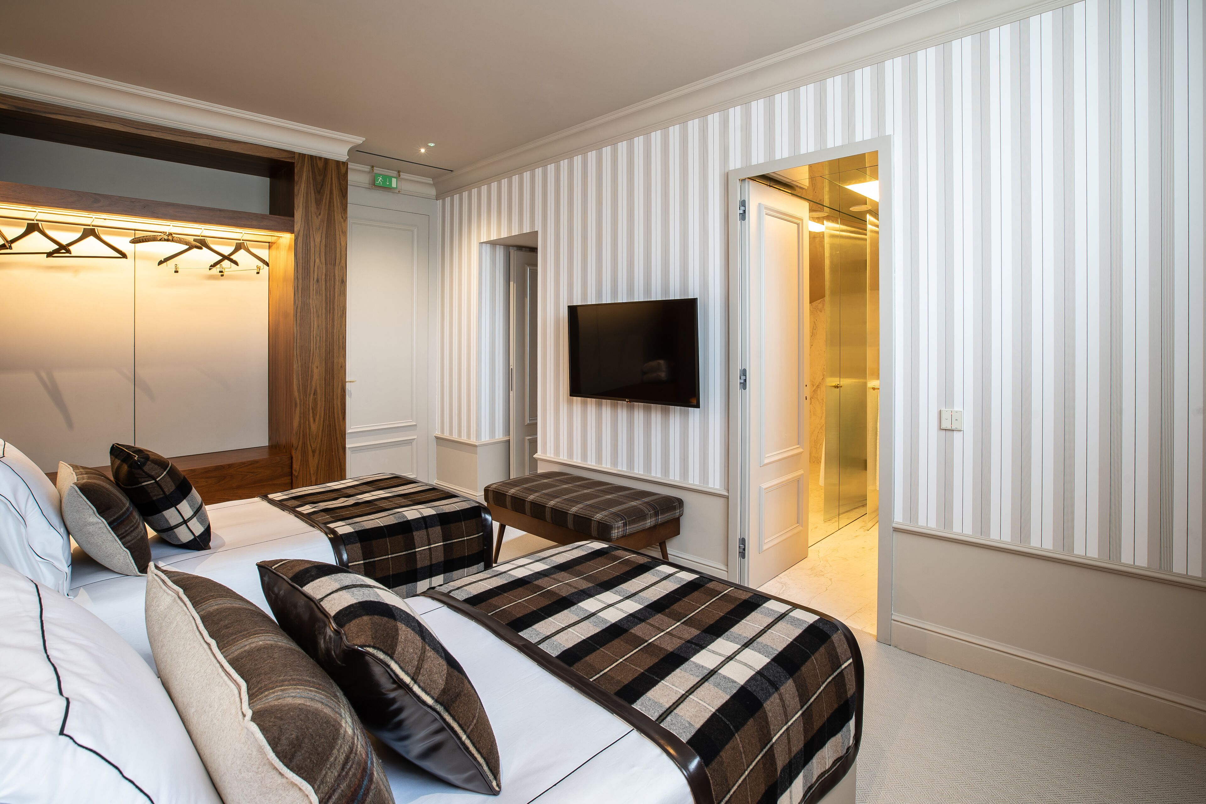 A hotel room with two beds, a flat-screen TV, a bench, and a walk-in closet.