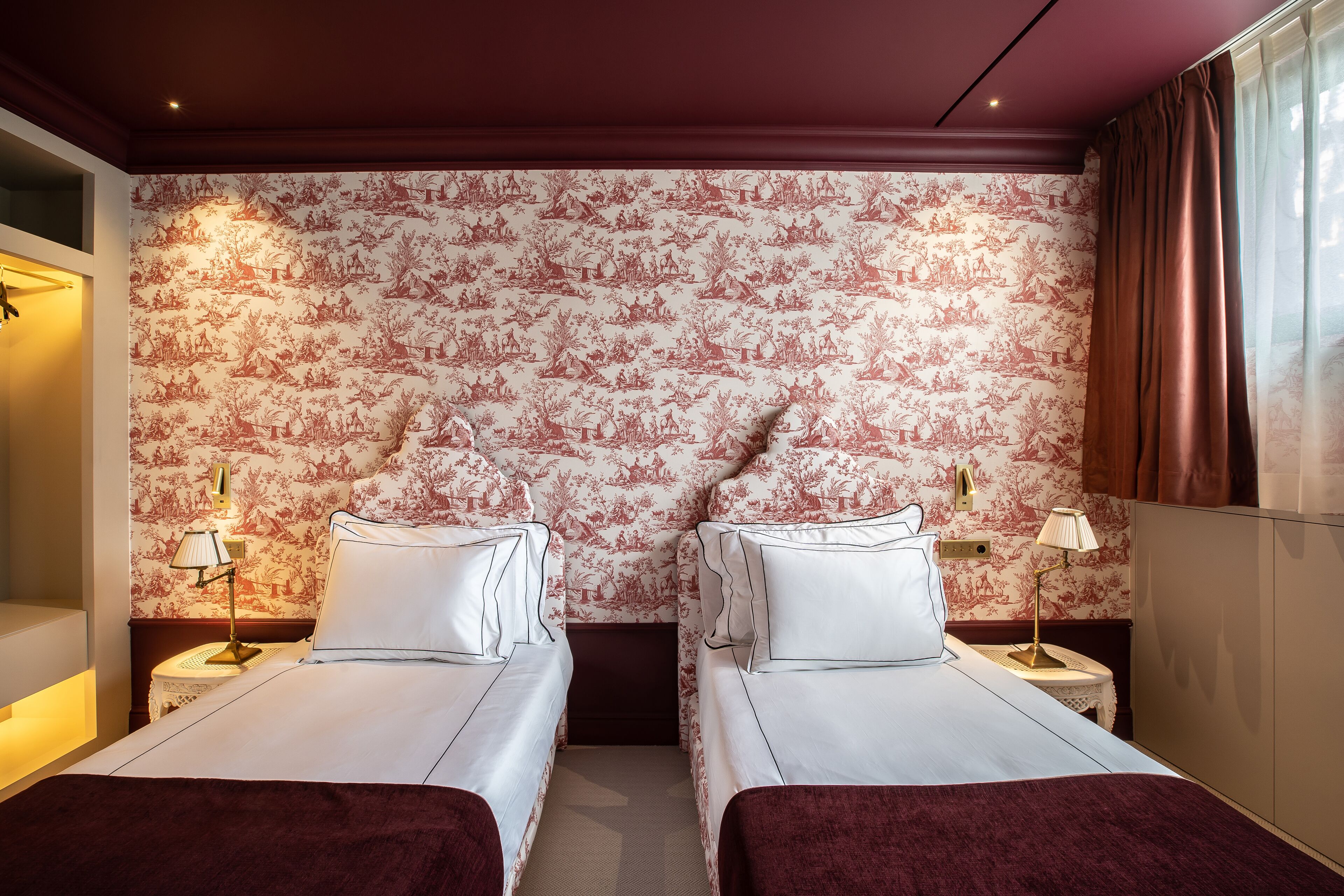 Ein Hotelzimmer mit zwei Betten, floralem Wanddesign, Nachttischlampen und einem Fenster mit Vorhängen.