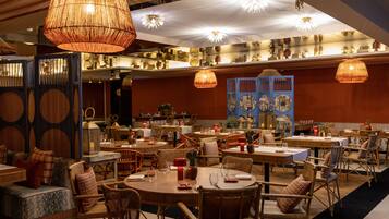 A restaurant with round tables, wicker chairs, and hanging lamps.