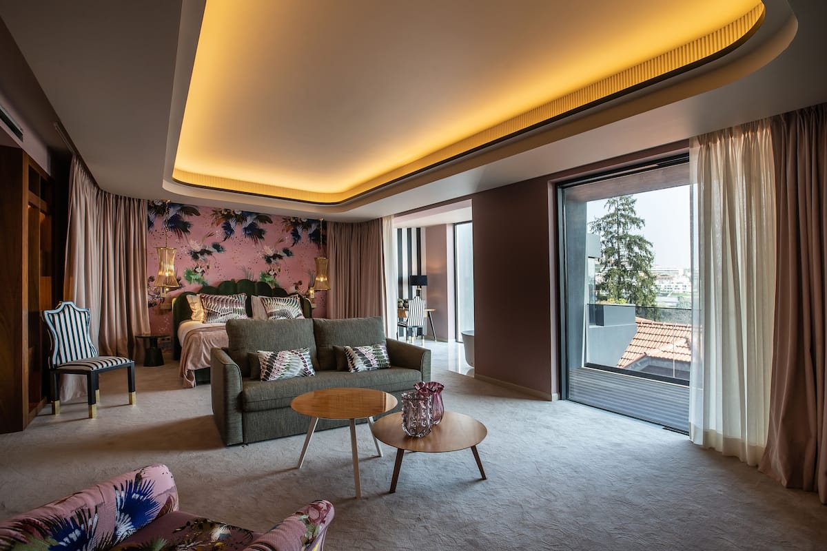 Un salon moderne avec un canapé, un fauteuil et une table basse ronde. On aperçoit un lit à baldaquin à l’arrière-plan.