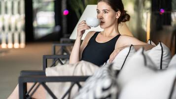 A person sitting on a black chair with a white pillow, holding a white cup.