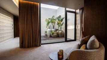 Een moderne woonkamer met een bank, een bijzettafeltje en uitzicht op een balkon met planten.