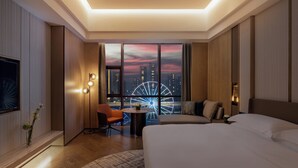 Une chambre d’hôtel avec un grand lit, un coin salon avec une table et une vue sur le paysage urbain, avec une grande roue en toile de fond.