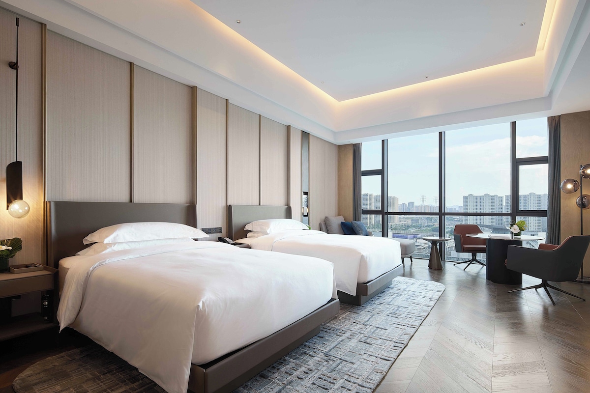 Une chambre d’hôtel moderne avec deux lits, un bureau et une vue sur la ville.