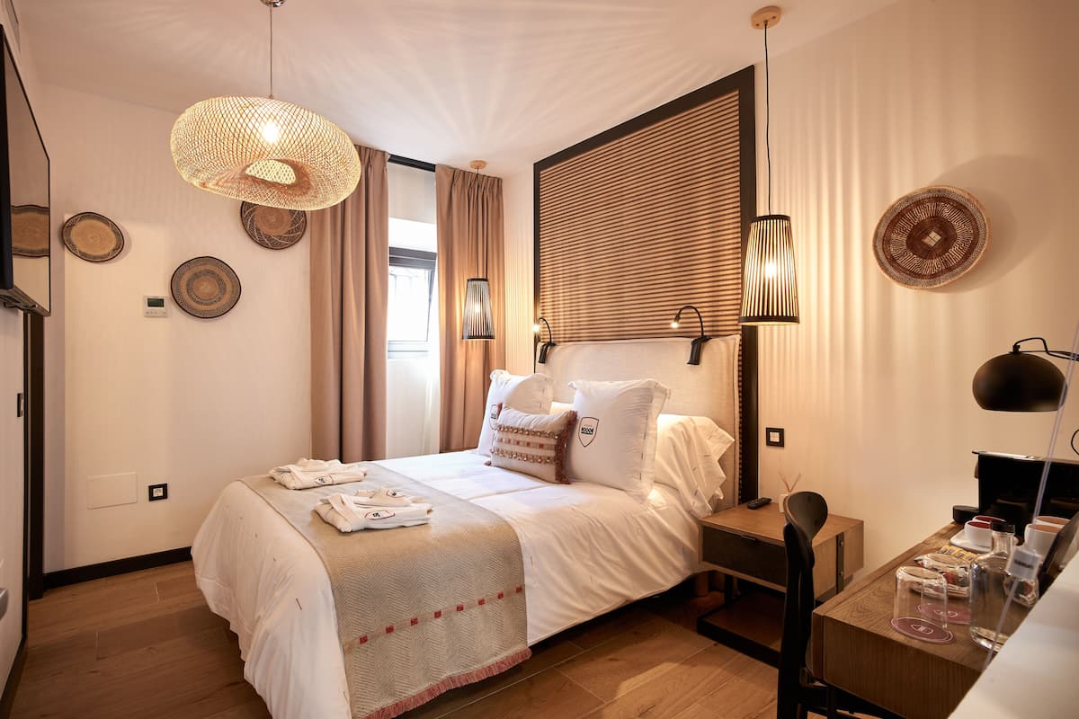 A neatly arranged hotel room with a bed, bedside table, and a desk with a chair.
