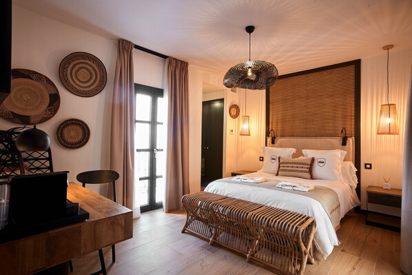 A modern bedroom with a large bed, a desk with a laptop, and a wicker bench.