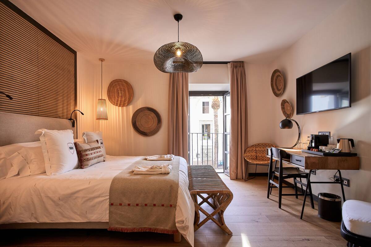A bedroom with a bed, bedside table, desk, chair, and a TV.