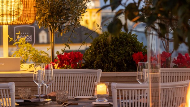 An outdoor dining area with wicker chairs, a table set with glasses and a candle, and a view of a building in the background. - Hotel Santo Cristo La Ciudadela Marbella (Marbella)