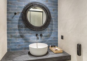 A bathroom with a round mirror, a white sink, and a blue-tiled wall. - SAVUS BOUTIQUE HOTEL (Rethymno)