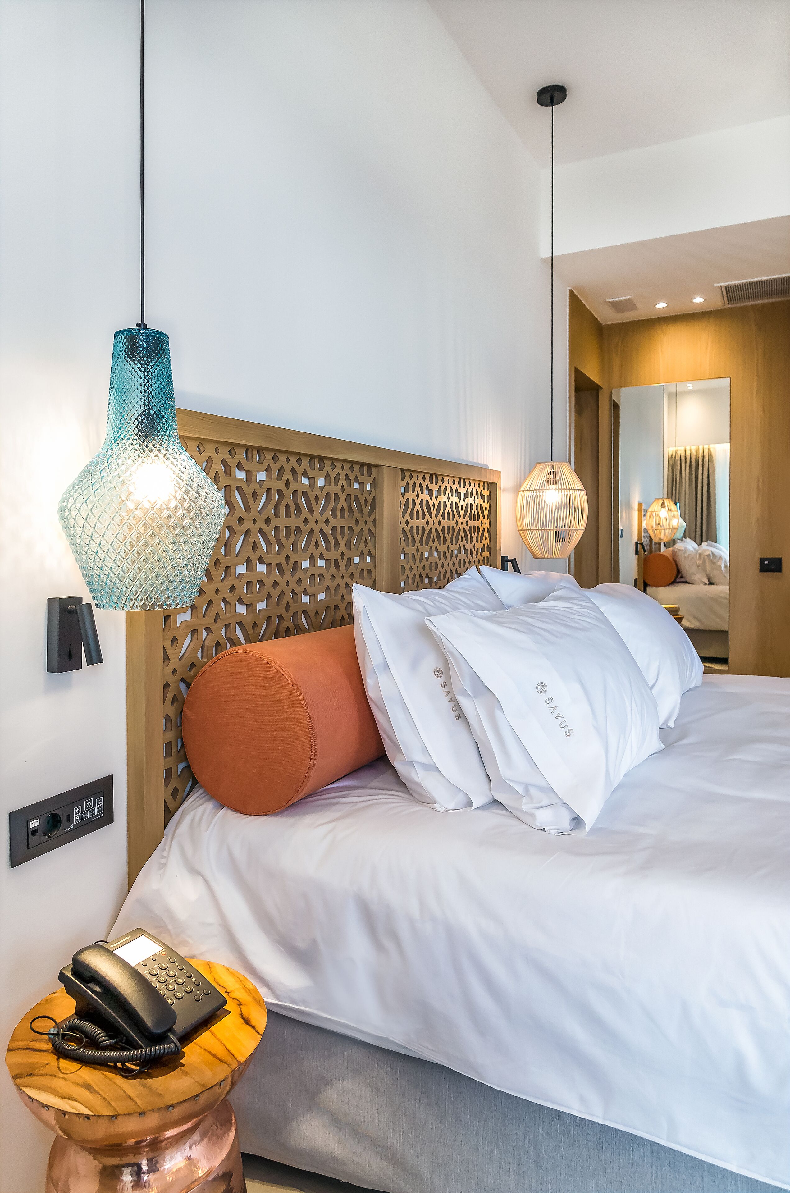 A modern hotel room with a wooden headboard, white bedding, and a telephone on a wooden side table.