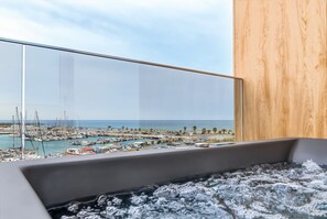 Et moderne badeværelse med et hjørnebadekar af glas med udsigt over en havn og havet.