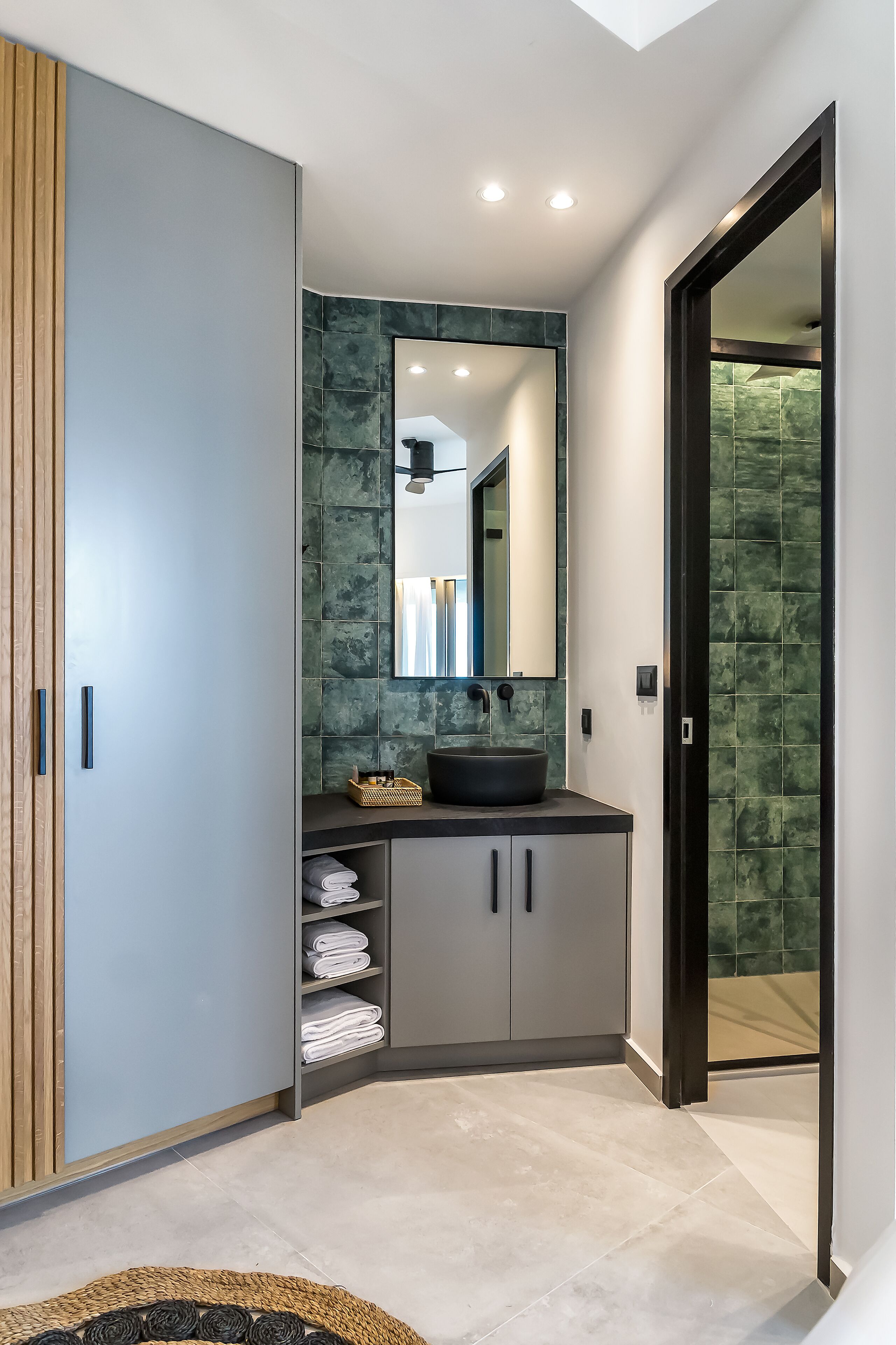 A modern bathroom with a large mirror, a round sink, and a built-in shelf with towels.