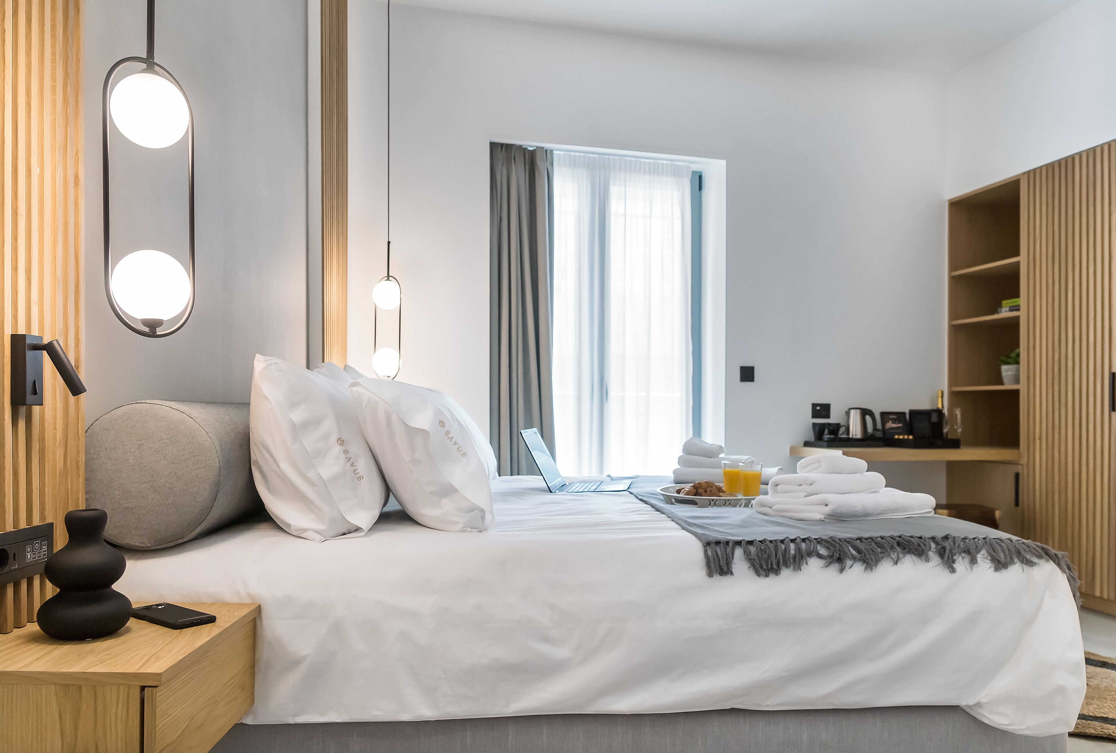 Et moderne hotelværelse med en pænt redt seng, et natbord med lampe, en bærbar computer og et morgenmadsmag.
