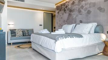 A modern hotel room with a large bed, a sofa, and a wooden side table.