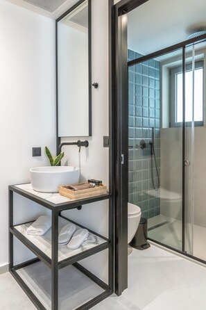 A modern bathroom with a white sink, a mirror, a glass shower enclosure, and a marble-tiled floor.