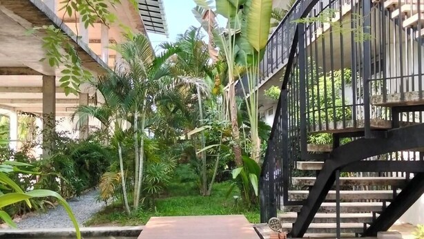 Eine Holzterrasse über einem Wasserspiel, umgeben von üppiger Bepflanzung und einer schwarzen Metalltreppe.