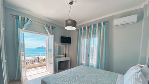 Ein Schlafzimmer mit einem Bett, einem Nachttisch, einem Spiegel und Meerblick durch eine geöffnete Tür.