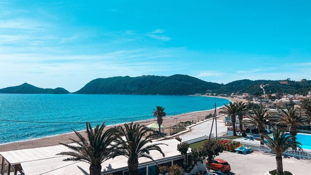 Blick auf die Küste mit Strand, Palmen und einem Poolbereich.