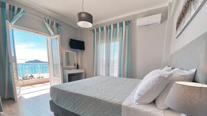 Ein Schlafzimmer mit Bett, Nachttisch, Lampe und einer offenen Tür, die auf einen Balkon mit Meerblick führt.