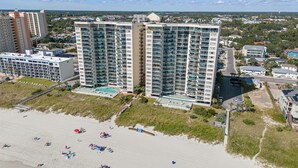A high-rise hotel with multiple balconies, a pool, and a beach area with umbrellas.