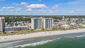 A coastal cityscape with high-rise buildings, a sandy beach, and a clear blue sky.