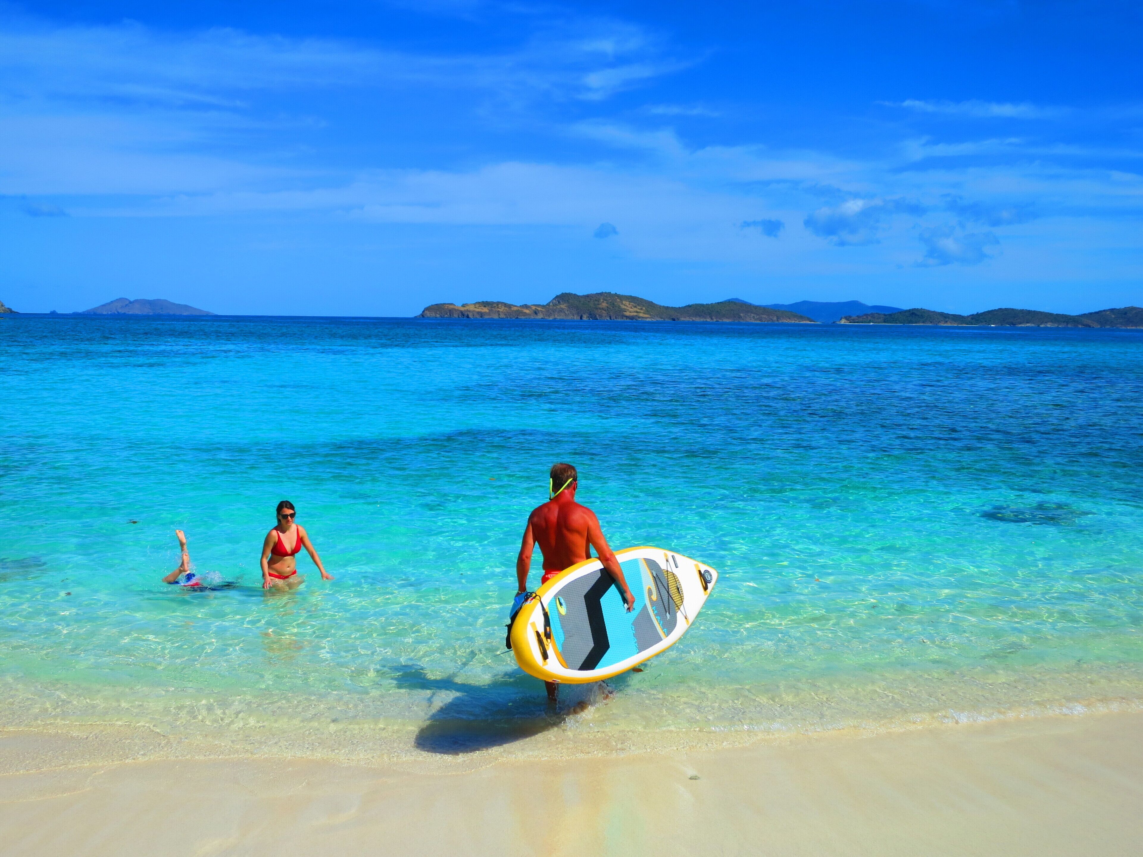A beach scene with clear turquoise water and distant mountains.