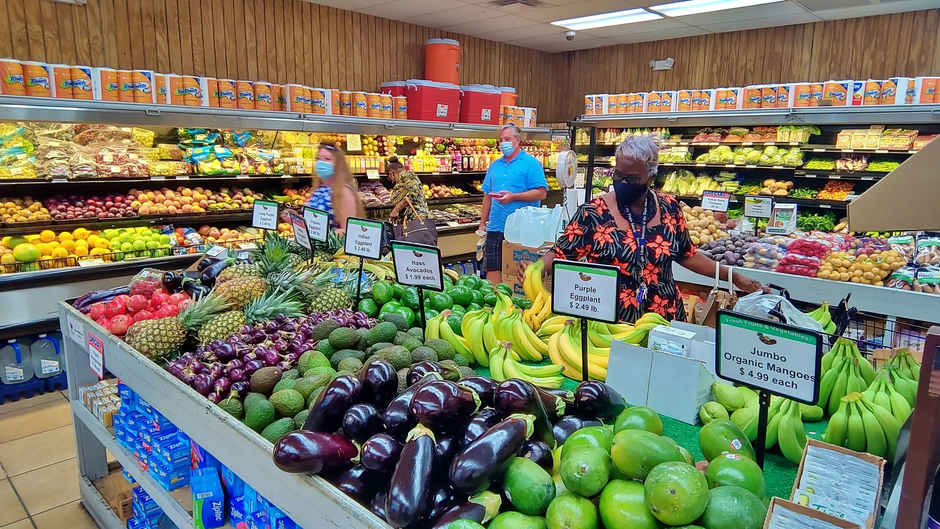 Une épicerie où sont exposés divers fruits et légumes, notamment des bananes, des avocats et des aubergines.