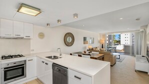 Eine moderne Küche mit weißen Schränken, einem Geschirrspüler und einem Herd. Es gibt einen Essbereich mit Tisch und Stühlen sowie eine Wohnbereich mit einer Couch und einem Couchtisch. Der Raum verfügt über ein großes Fenster mit Blick auf Gebäude.