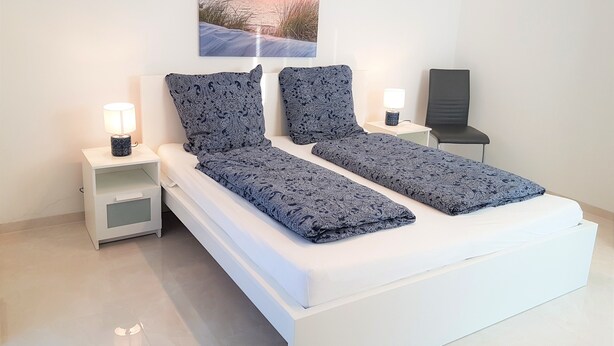 Een moderne slaapkamer met een bed, twee nachtkastjes, een stoel en een aan de muur hangend schilderij.