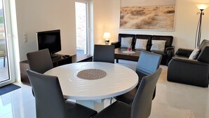 Een moderne woonkamer met een ronde eettafel, zwarte leren banken, een flatscreen-tv en een groot landschap op de muur.