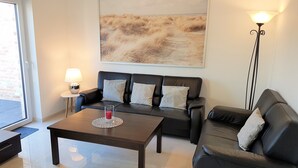 Een moderne woonkamer met een zwarte leren bank, een houten salontafel met een rode kaars, een vloerlamp en een groot abstract schilderij aan de muur.