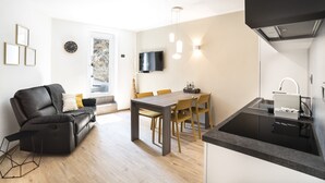 Un espacio habitable moderno con zona de comedor, cocina con encimera negra y sofá negro con cojines.