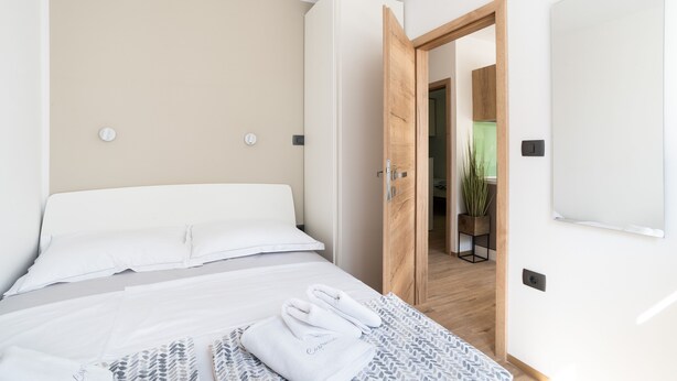 Una habitación de hotel moderna con una cama bien hecha, una puerta de madera que da a un baño y una pequeña planta en maceta.
