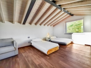 Une chambre moderne avec un plafond en pente, deux lits, un petit canapé et une fenêtre donnant sur un paysage verdoyant.