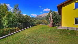 A grassy yard with a yellow building, a fenced area, and trees. - Rosalba, Private solar heated pool, walk restaurants, romantic, mountain views.  (Corfino)