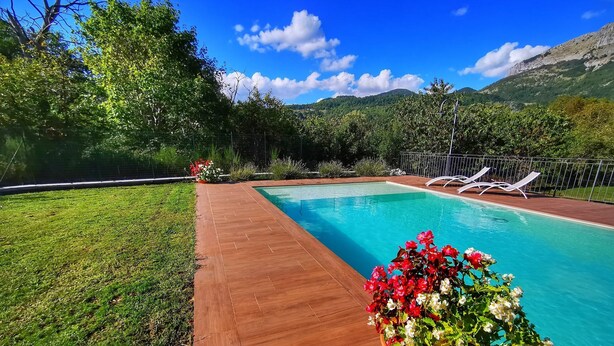 A rectangular swimming pool with a wooden deck, surrounded by lush greenery and a mountainous backdrop. - Rosalba, Private solar heated pool, walk restaurants, romantic, mountain views.  (Corfino)