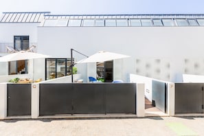 A modern outdoor area with a glass wall, two white umbrellas, and a seating area with a table and chairs. - Heroismo Duplex Terrace (Porto)