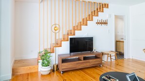 Een moderne woonkamer met een houten trap, een flatscreen televisie op een houten dressoir en een kamerplant.