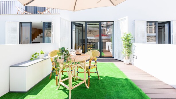 Een terras buiten met een tafel, stoelen en een grote parasol.